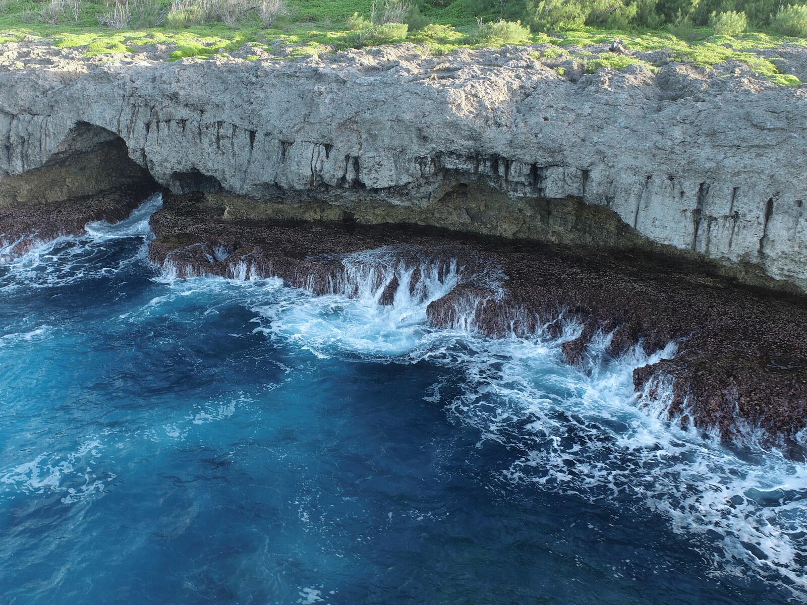 Breaking turquoise waves beneath the pale limestone cliff at Totiko, Atiu.